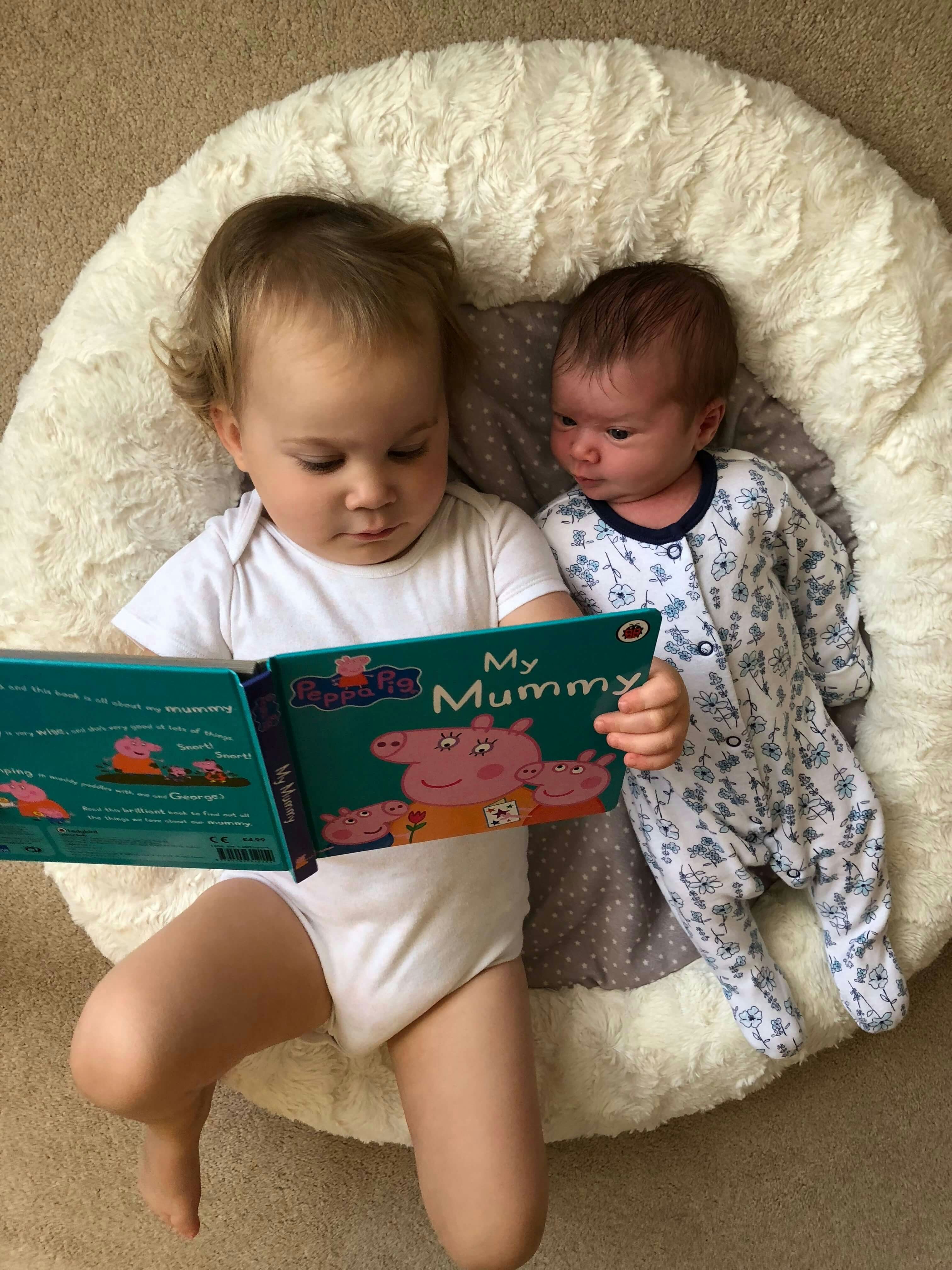 A toddler reads a book to her baby sister