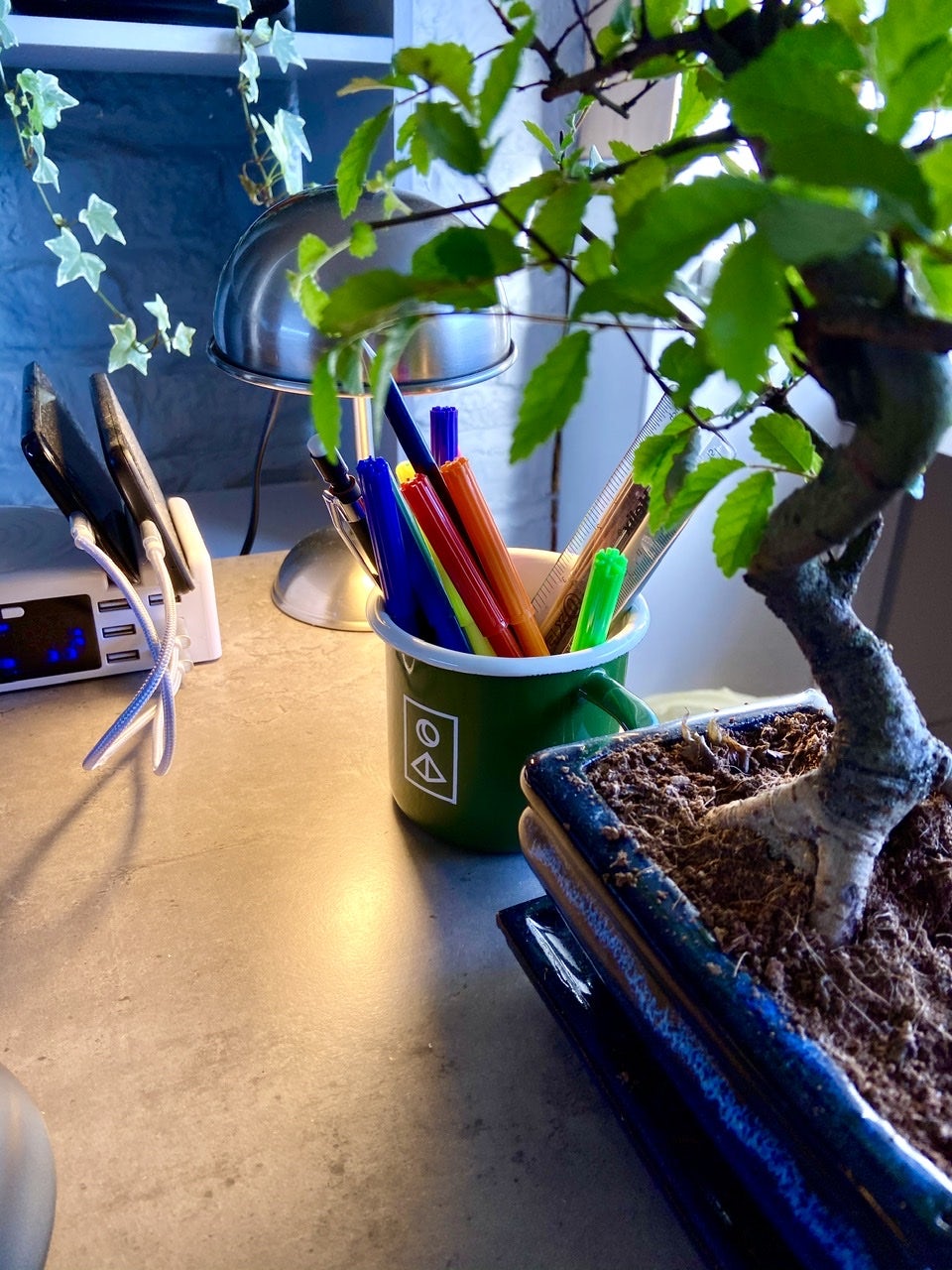 A green Faculty branded cup with various pens in it