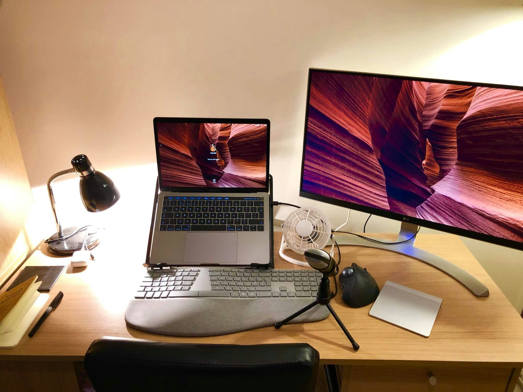 An office desk with a mounted MacBook Pro, an external display and various accessories